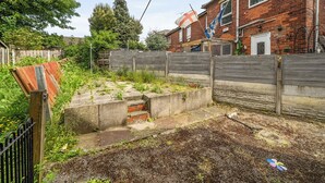 A residential backyard with a brick house, a wooden fence, and a flag. - 2 Bed House - Sleeps 4 - Parking - Wifi (Sheffield)