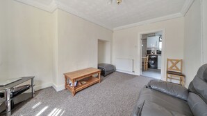 A living room with a leather sofa, a wooden coffee table, a small TV stand, a grey sofa, and a wooden chair. - 2 Bed House - Sleeps 4 - Parking - Wifi (Sheffield)