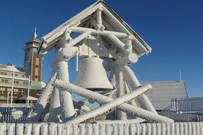 Eine große, mit Schnee bedeckte Glockenturmanlage, im Hintergrund ein Gebäude und ein weiterer Turm.