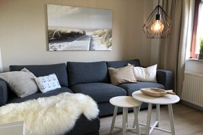 Ein Wohnzimmer mit einer Couch, einem weißen, flauschigen Teppich, einem runden Tisch mit einer Schale und einer Pendelleuchte.