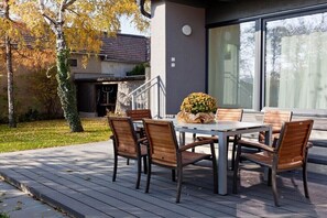 Un patio al aire libre con una mesa y sillas, un pequeño jardín y un edificio con un ventanal grande.