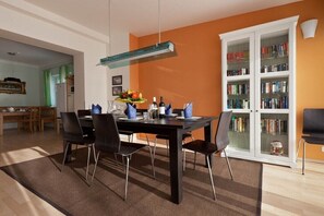 Un comedor con una mesa dispuesta para cuatro, sillas, una estantería y una cocina al fondo.
