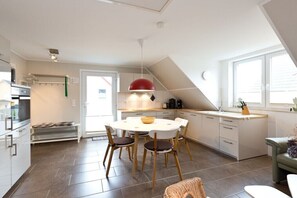 A modern kitchen with a dining area, white cabinetry, a red pendant light, and a view of the outside. - Holiday apartment Stieglitz View (Röbel\/Müritz)