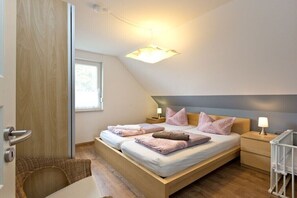 A bedroom with a bed, bedside tables, a lamp, a crib, and a window. - Holiday apartment Stieglitz View (Röbel\/Müritz)