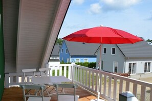 A covered outdoor area with a table and chairs, a red umbrella, and a view of houses in the background. - Holiday apartment Stieglitz View (Röbel\/Müritz)