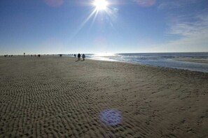 Ein breiter Sandstrand mit Fußspuren, ein klarer Himmel und die Sonne scheint.