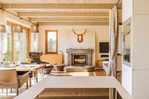 Ein modernes Interieur mit Kamin aus Stein, Holzbalken, Essbereich und großem Fenster.