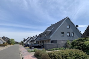 Eine Wohnstraße mit Häusern, parkenden Autos und blauem Himmel.