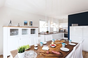 Eine moderne Küche mit weißen Schränken, einem Holztisch und Pendelleuchten.