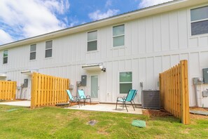 A two-story building with a white exterior, a covered patio area with chairs, and a wooden fence. - Lost Bay Hideaway (Orange Beach)