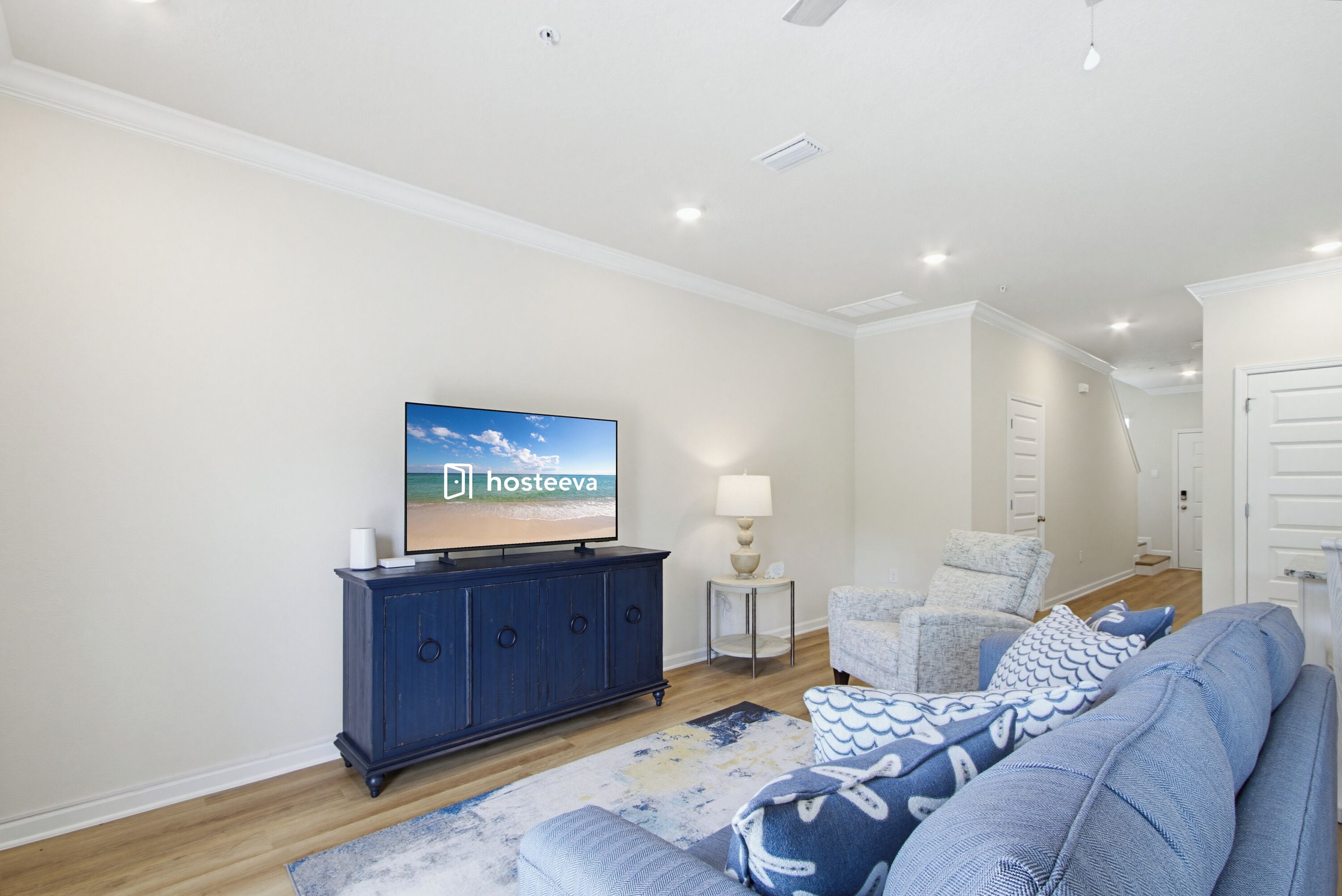 A modern living room with a television, a blue sofa, a small side table with a lamp, and a patterned rug.
