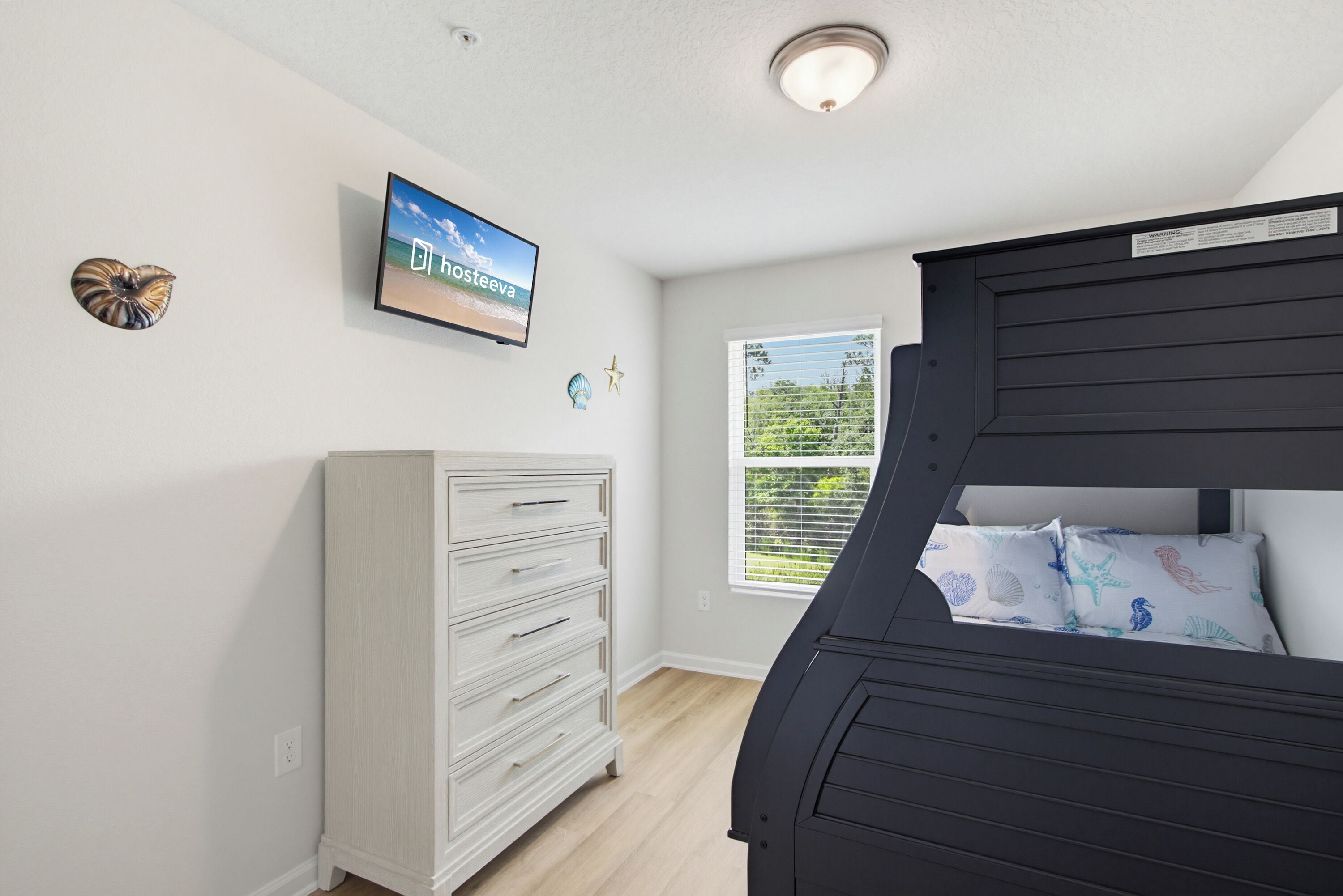 A bedroom with a bunk bed, a dresser, a television, and a window with blinds.