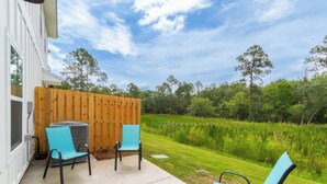 Un patio al aire libre con dos sillas y una mesa, una valla de madera y vistas a un campo verde y árboles.