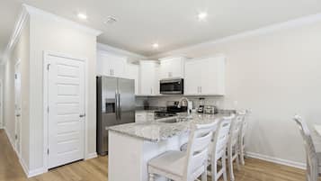 A modern kitchen with white cabinetry, a granite countertop, stainless steel appliances, and a bar seating area.