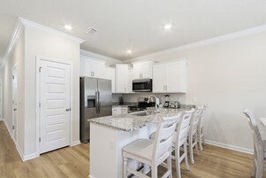 A modern kitchen with white cabinetry, a granite countertop, stainless steel appliances, and a bar seating area.