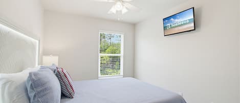 A bedroom with a bed, pillows, a ceiling fan, a TV, and a window with blinds.