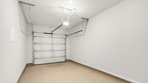 Una habitación limpia y vacía con una puerta de garaje de estructura metálica, paredes blancas y piso color beige.