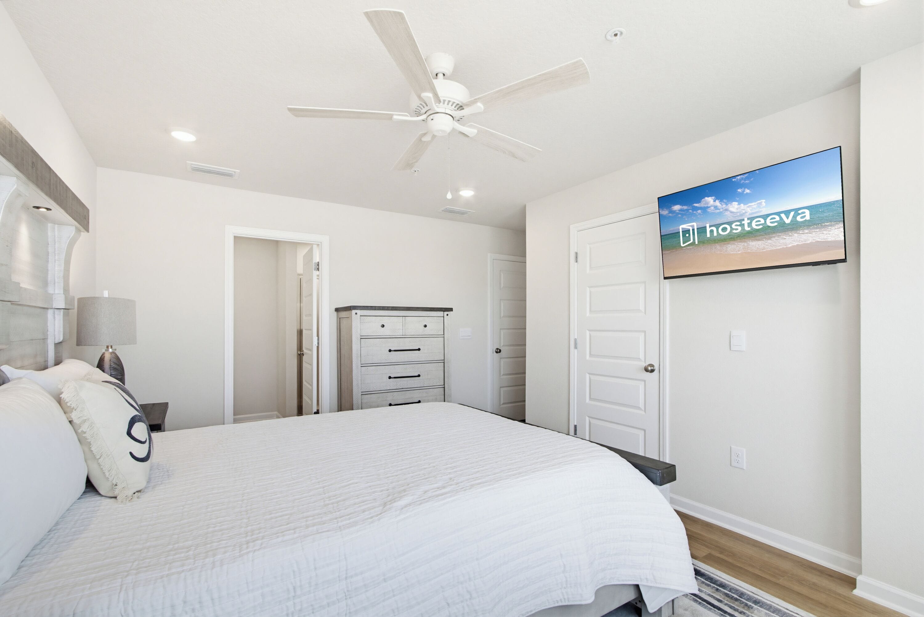 A bedroom with a bed, a ceiling fan, a TV on the wall, and a dresser.