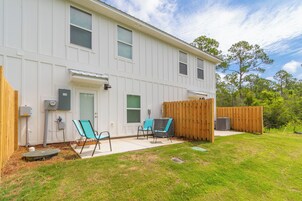 A white two-story building with a covered patio area, a wooden fence, and a grassy yard.