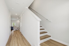 A hallway with wooden flooring, white walls, and a staircase with wooden steps and white railings. - Lost Bay Hideaway (Orange Beach)