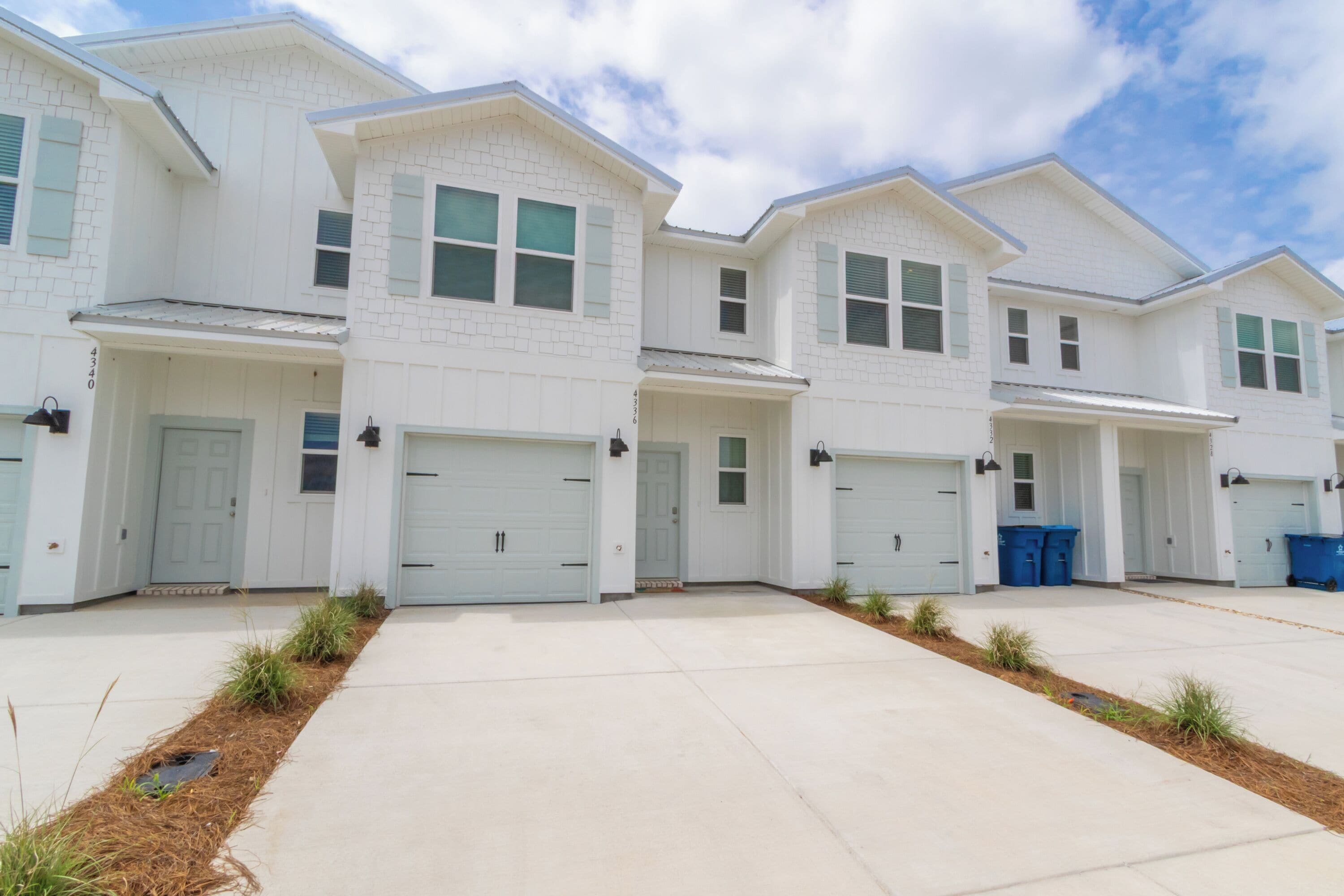 A row of white two-story houses with garage doors, a clear sky, and a well-maintained lawn.
