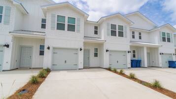 A row of white two-story houses with garage doors, a clear sky, and a well-maintained lawn.