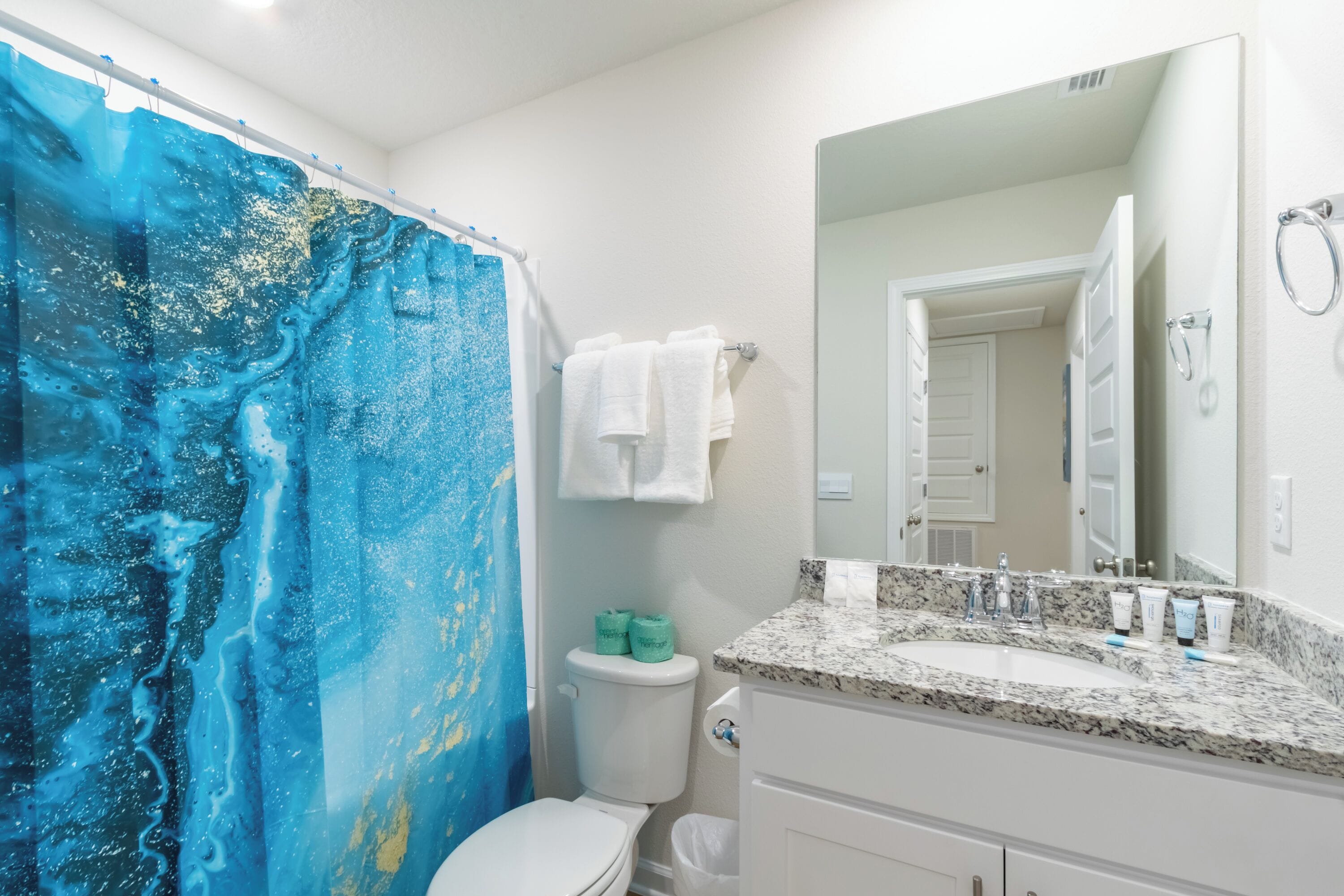 A bathroom with a shower curtain, toilet, sink, and mirror.