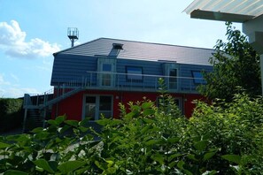 A two-story building with a red and blue exterior, a metal roof, and a staircase leading to a balcony. - Fewotraum-Müritz "Möwe 2" (Röbel\/Müritz)