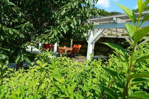 A covered outdoor seating area with a table and chairs, surrounded by lush greenery. - Fewotraum-Müritz "Möwe 2" (Röbel\/Müritz)
