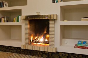 A fireplace with a stone surround, bookshelves above, and a Monopoly game box on the lower shelf. - Rheinsberg in the Lexow Manor House (Walow OT Lexow)