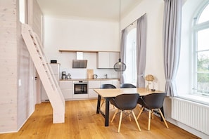 A compact kitchen with a dining area, wooden flooring, and a window with curtains. - Holiday apartment with 1 bedroom (Steinberg)