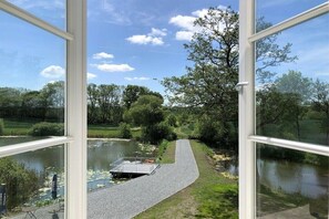 A view through a window of a pathway leading to a dock over a body of water, surrounded by trees and greenery. - Holiday apartment with 1 bedroom (Steinberg)
