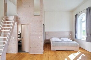 Ein Schlafzimmer mit einer Holztreppe, einem Bett, einem Fenster mit Vorhängen und Blick ins Freie.