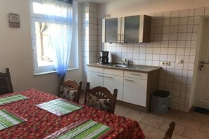Eine kleine Küche mit weißen Schränken, einer Kaffeemaschine und einem Papierkorb.