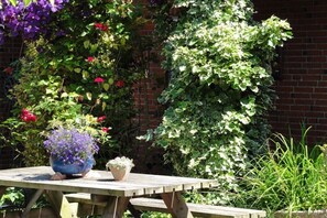 Ein Holztisch mit Blumentöpfen, eine Ziegelwand und ein Garten mit verschiedenen Pflanzen und Blumen.