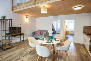 Ein moderner Wohnraum mit Essbereich, einer Couch, einem Fernseher und einer Küche.