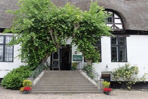 Ein traditionelles Gebäude mit einem Reetdach, einer Treppe zum Eingang und einem Schild, das ein Restaurant kennzeichnet.