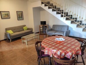 Ein Wohnzimmer mit einer Couch, einem Couchtisch, einem Esstisch mit Stühlen, einer Treppe und zwei gerahmten Bildern an der Wand.