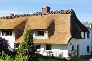 Ein Haus mit Strohdach, weißen Wänden und einem Schornstein.