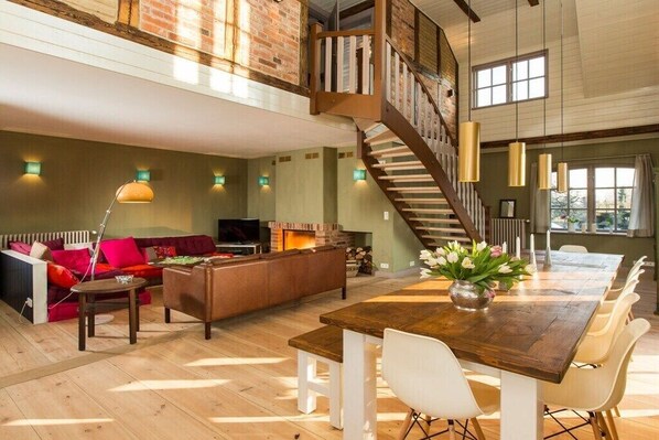 Ein geräumiges Loft mit hohen Decken, freiliegenden Backsteinwänden, einer Holztreppe und einer gemütlichen Sitzecke mit Kamin.