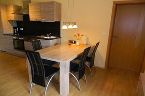 Eine moderne Küche mit Holzausstattung, integriertem Backofen, einem Esstisch mit Stühlen und Pendelleuchten.