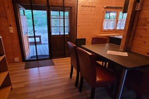 Eine Holzhütte mit Essbereich, einem großen Fenster und einer Tür, die nach draußen führt.