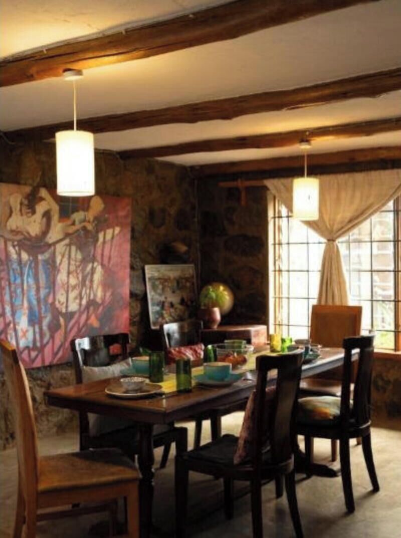 A dining area with a wooden table and chairs, stone walls, and a large painting.