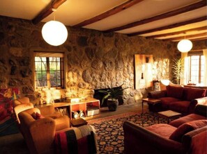 A rustic living room with stone walls, wooden beams, a fireplace, and a large window. - Oloile - Home By The Park (Nairobi)