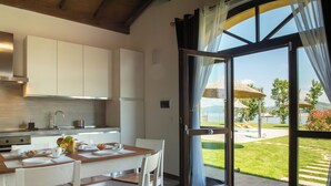 A modern kitchen with white cabinets, a dining table with chairs, and a large sliding glass door leading to a patio with umbrellas. - Villa with pool and garden on Lake Trasimeno (Magione)