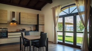 A modern kitchen with wooden cabinets, a dining table with chairs, and large windows with curtains. - Villa with pool and garden on Lake Trasimeno (Magione)