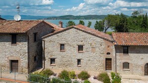 A stone building with a tiled roof, a satellite dish, and a view of a lake and mountains. - Villa with pool and garden on Lake Trasimeno (Magione)