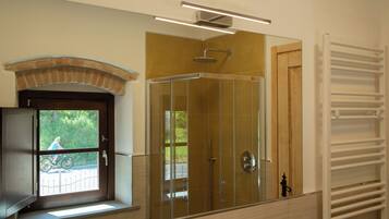 Une salle de bain avec une douche à parois de verre, une fenêtre donnant sur une personne à vélo et un porte-serviettes blanc.