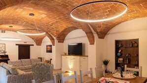 A living room with a brick ceiling, a television, a dining table with a tray, and a bookshelf. - Villa with pool and garden on Lake Trasimeno (Magione)