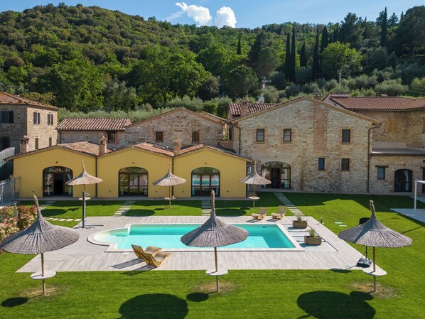 A large stone building with a swimming pool, surrounded by a well-maintained lawn and outdoor seating.